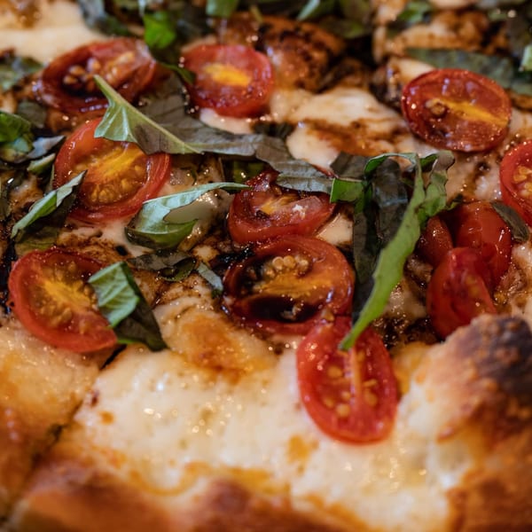 Close-up of a Fat Kid Woodfired Pizza with cherry tomatoes, fresh basil, and mozzarella cheese.