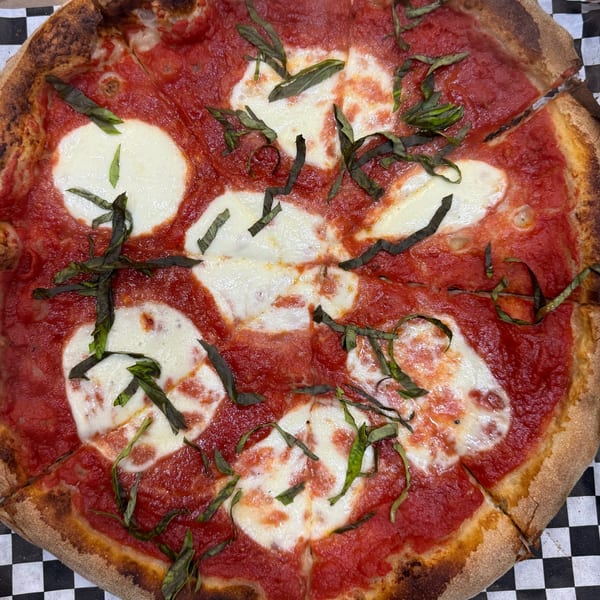 A close-up of a Fat Kid Woodfired Pizza Margherita pizza with fresh basil, mozzarella, and tomato sauce.