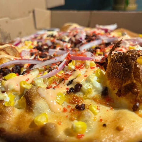 Close-up of a Fat Kid Woodfired Pizza with corn, red onions, and a creamy sauce.