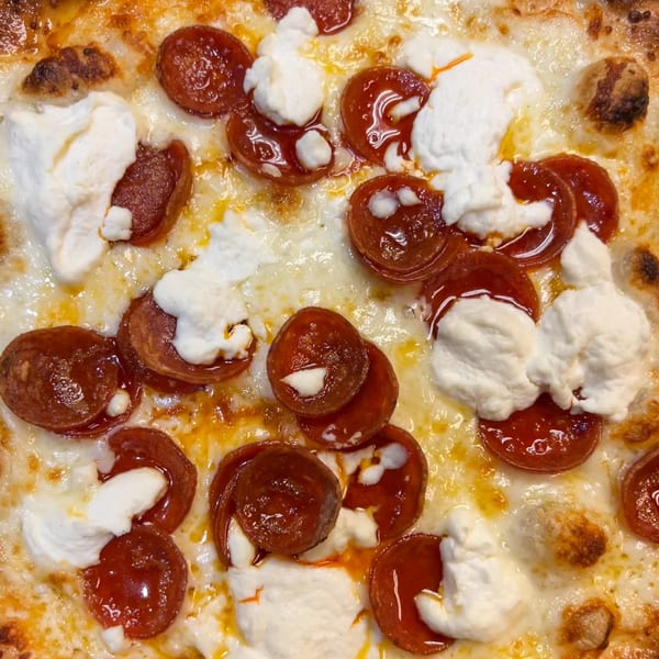 Close-up of a Fat Kid Woodfired Pizza with pepperoni, melted cheese, and dollops of ricotta.