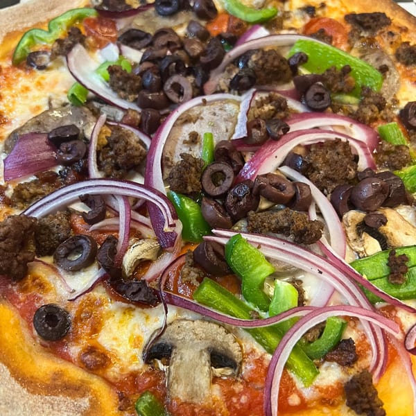 Close-up of a Fat Kid Woodfired Pizza with green peppers, red onions, black olives, and sausage.
