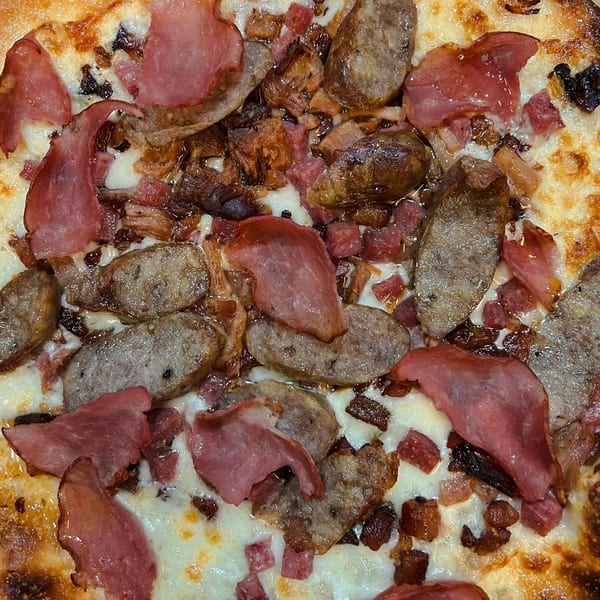 Close-up of a Fat Kid Woodfired Pizza with sausage, ham, and bacon on melted cheese.