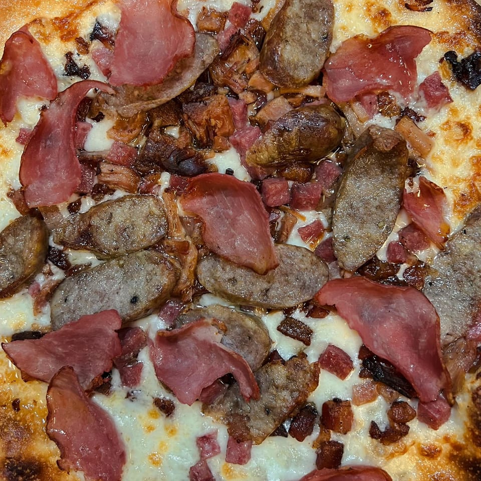 Close-up of a Fat Kid Woodfired Pizza with sausage, ham, and bacon on melted cheese.