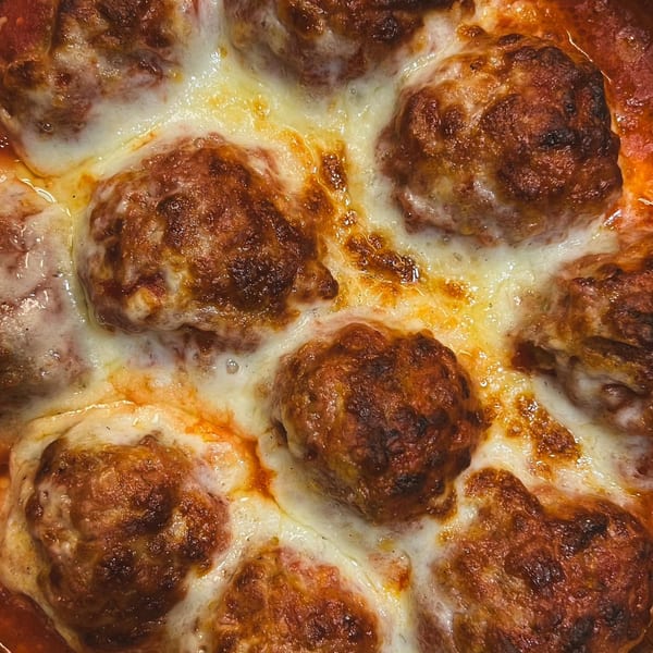 Close-up of baked meatballs covered in melted mozzarella cheese and tomato sauce.