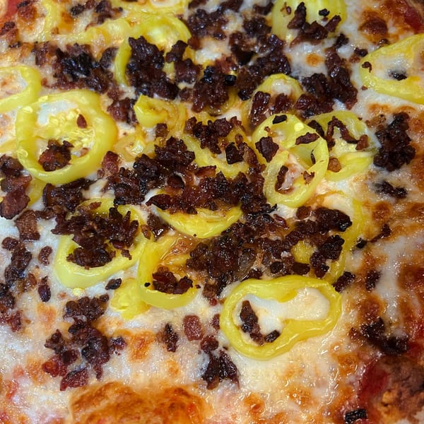 Close-up of a Fat Kid Woodfired Pizza with melted cheese, yellow peppers, and crumbled meat.